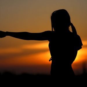 golden sunset with the silhouette of a woman in the foreground punching her arm out to the left