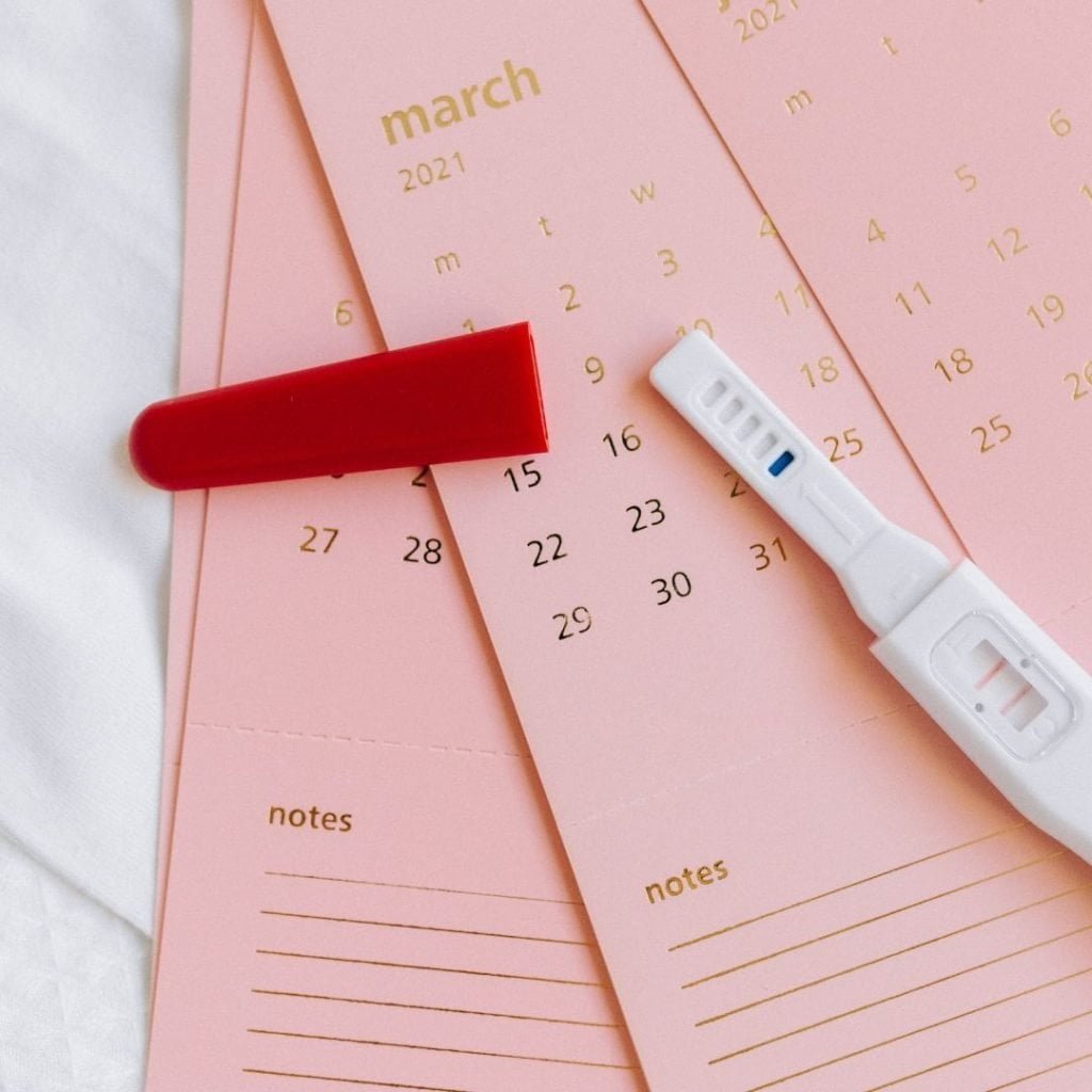 pink calendar sheets with a positive pregnancy test on top