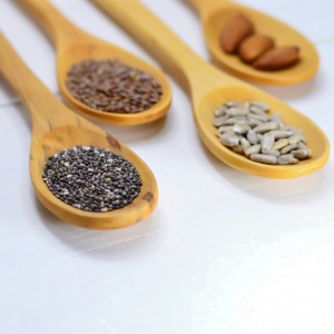 4 wooden tablesoons on a white table top with chia seeds, flax seeds, sunflower seeds, and almonds