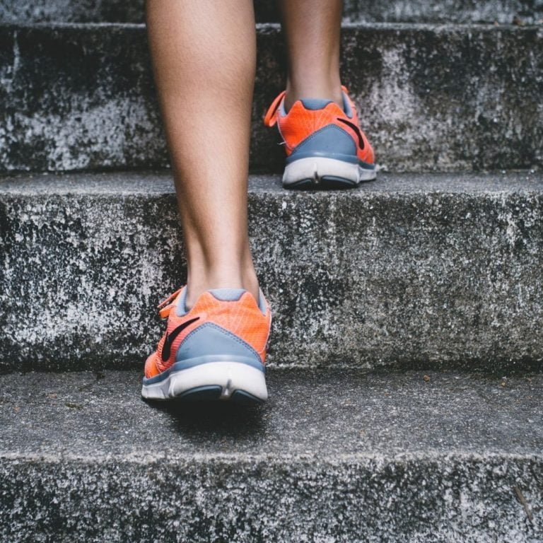 Legs from the calves down climbing up concrete stairs in grey and orange shoes