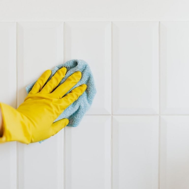 yellow gloved hand with a blue cleaning cloth on white tile