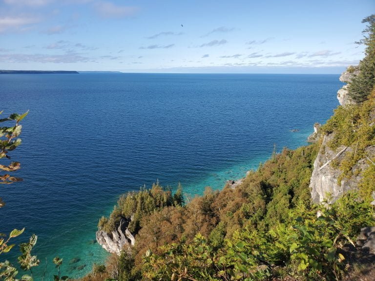 Blue water under a blue sky with white cliffs and green trees on the right side