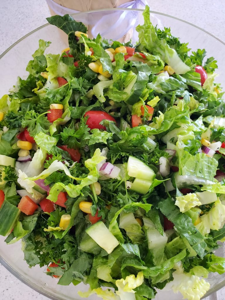 clear bowl with salad containing lettuce, onion, tomato, cucumber, parsley