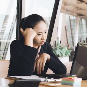 Asian woman sitting with her head in her hands at a desk