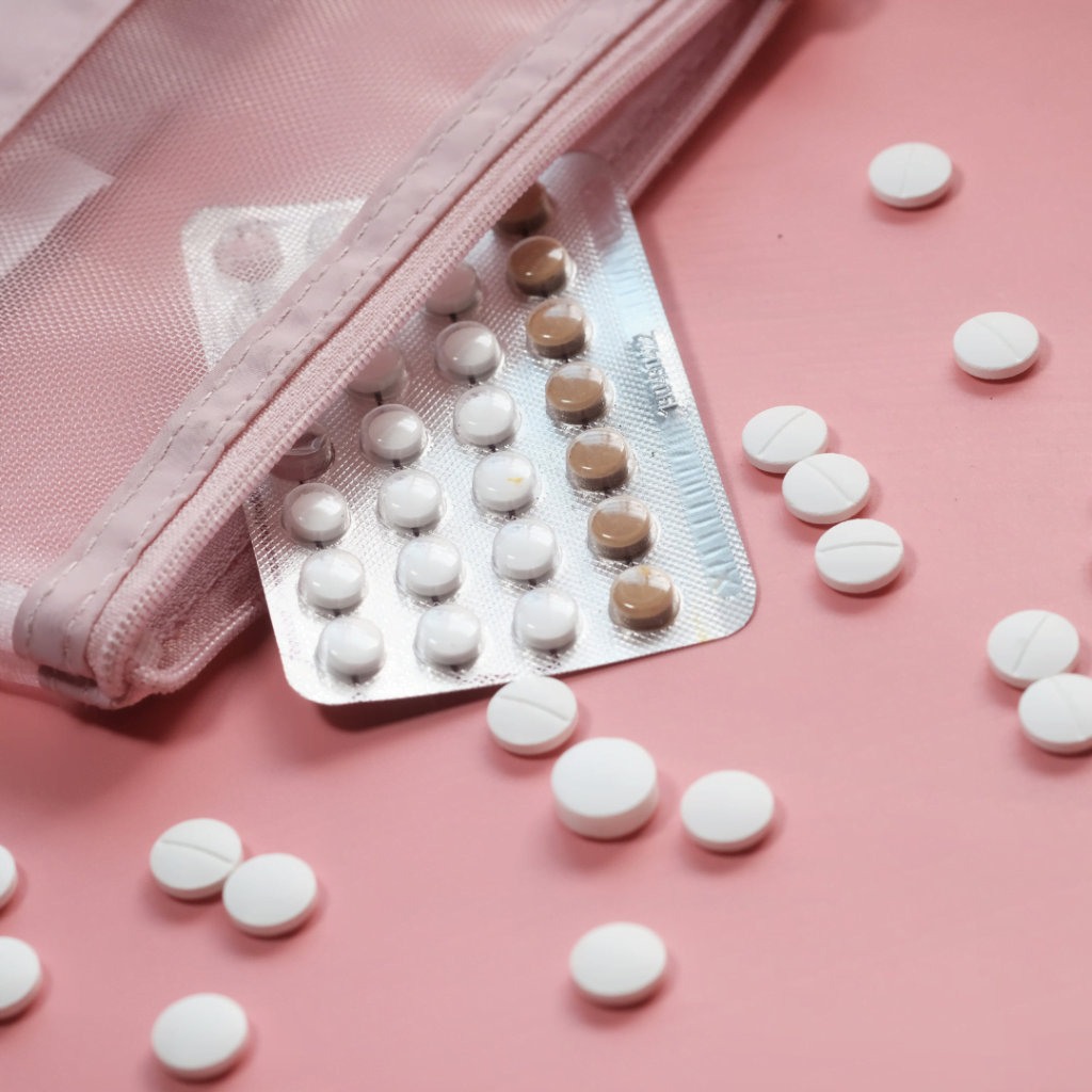 pink background with a pouch spilling a blister pack of oral contraceptive pill. White tablets are scattered on the pink background as well.