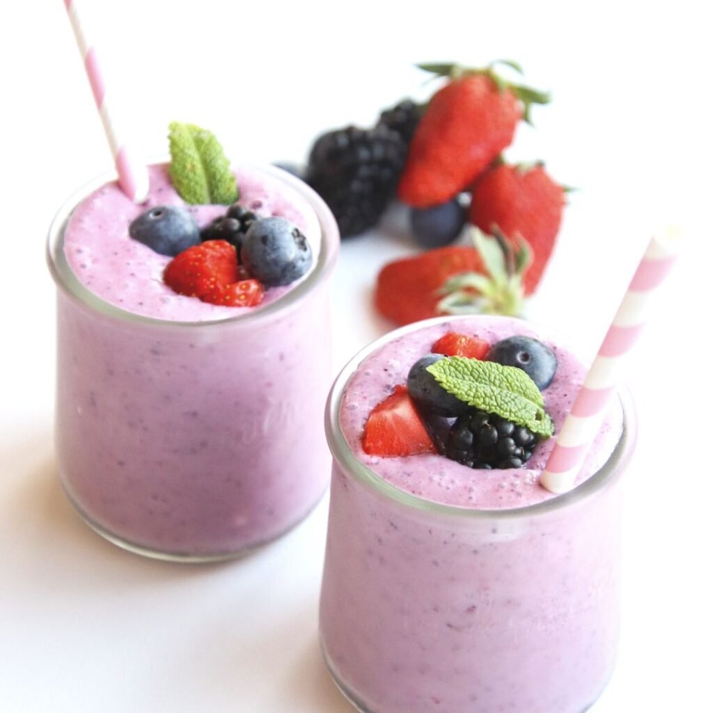2 small glasses filled with purple smoothie topped with berries and a straw sticking out.