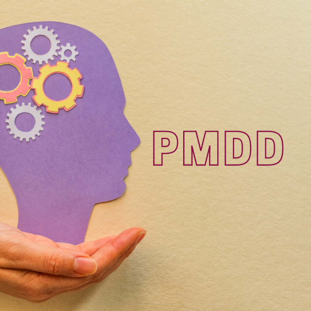 hand holding a head with cogs in the brain. The word PMDD is beside it.