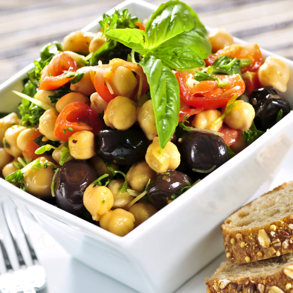 a white square bowl full to the brim with chickpea salad and topped with tomato and basil.
