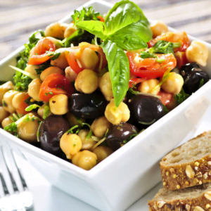 a white square bowl full to the brim with chickpea salad and topped with tomato and basil.