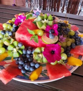 platter on a wood table with an assortment of colourful summer fruits: watermelon, blueberries, mango, kiwis, and grapes
