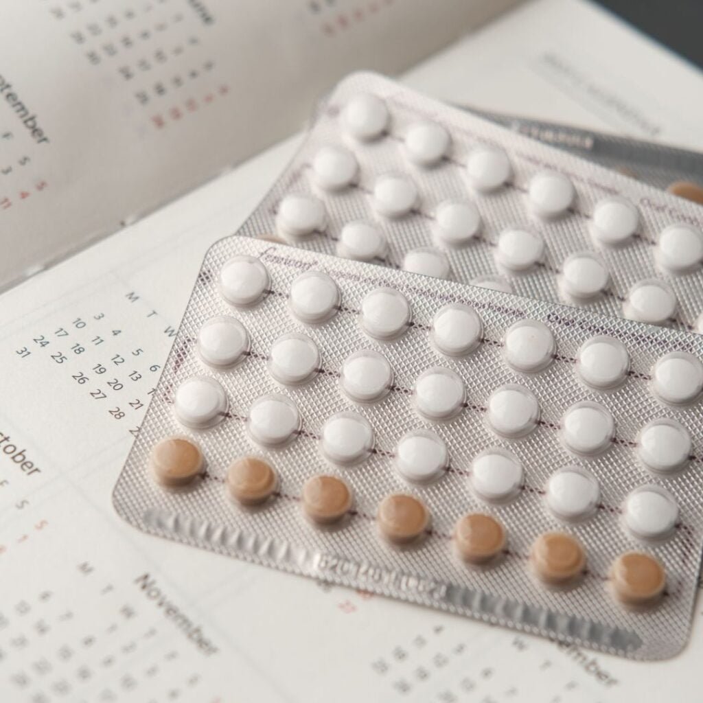 2 blister pack of oral contraceptives (21 white tablets, 7 brownish tablets) on top of an in-book calendar.