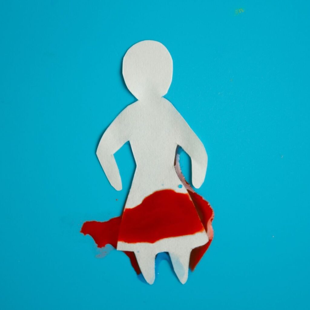white paper cutout of a person wearing a dress with blood across the skirt portion. Blue background.