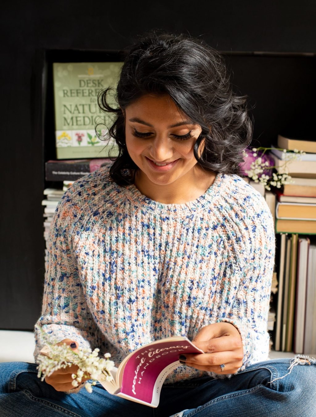 Anne Hussain on floor with book Dr. Anne, Newmarket Naturopath, sitting cross-legged on the floor reading a book on periods.